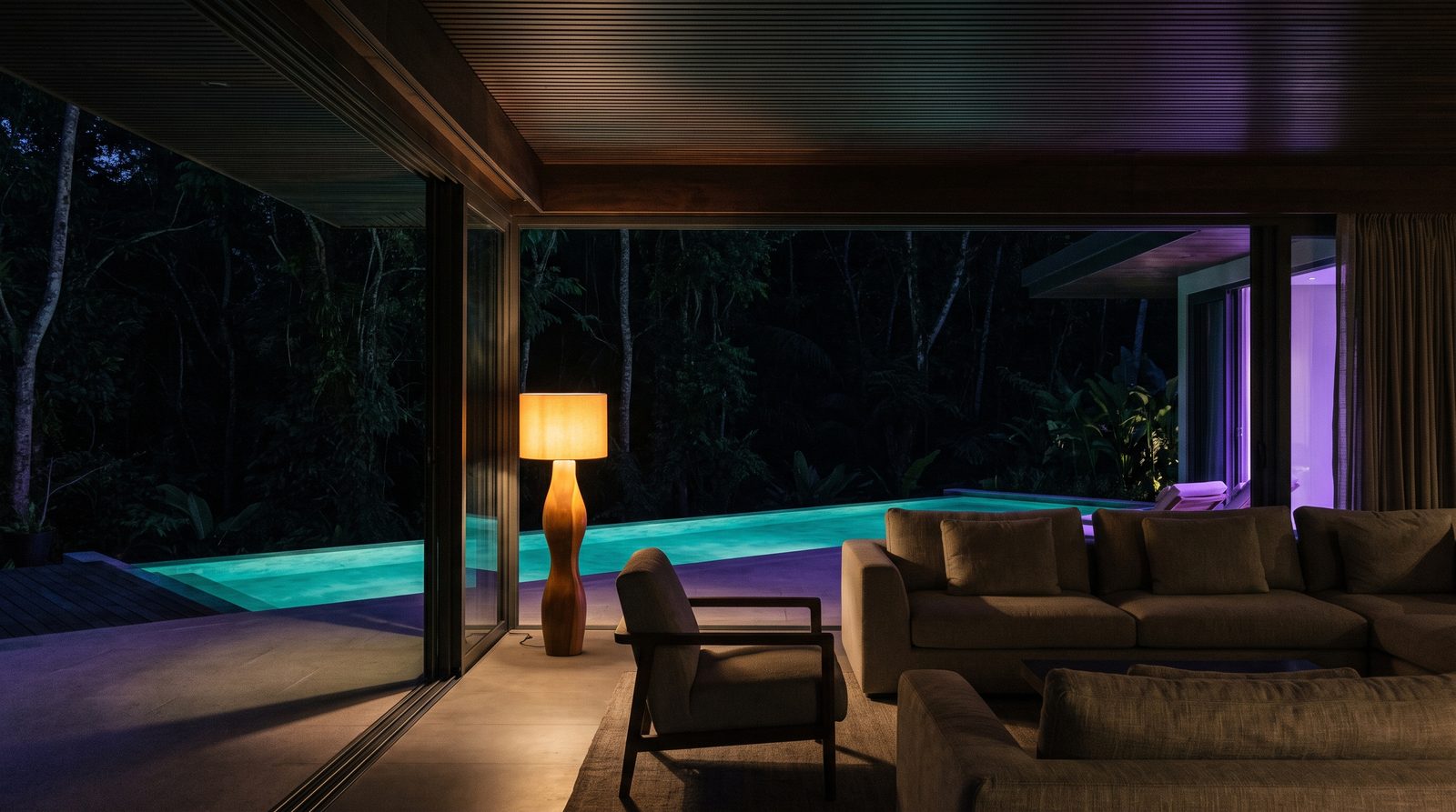 Interior de villa boutique tropical de noche, con vista a una piscina termal iluminada